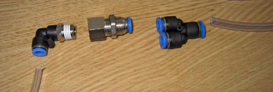A push-fit elbow and two push-fit connectors with blue collars and a length of clear tube, on a wooden table