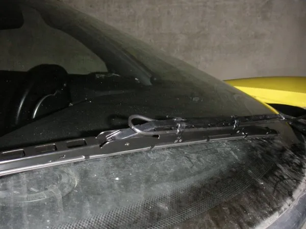 A wiper arm lying on a wet windscreen with a spray bar and tube looped near its base