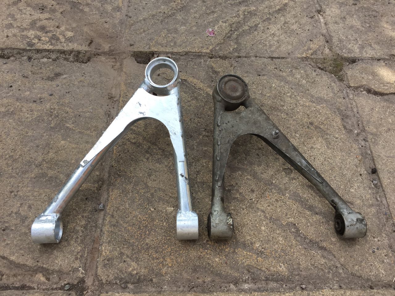 A home-built front upper wishbone laid next to an original wishbone on paving slabs